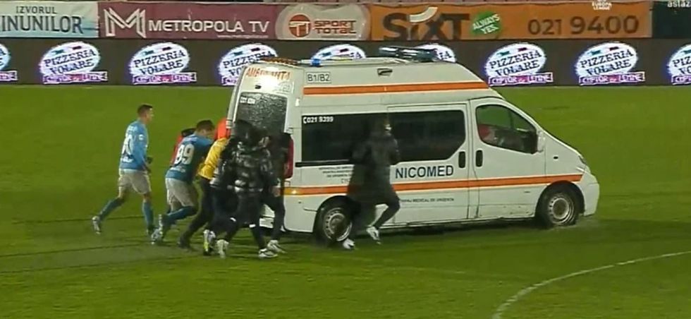 Lojtarët në Rumani shtyjnë ambulancën e bllokuar në fushë të shkatërruar nga shiu